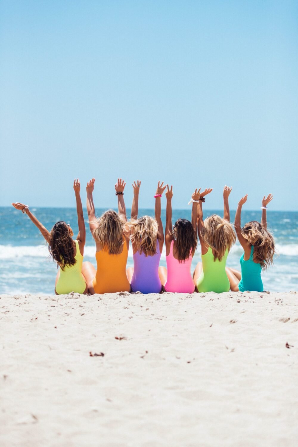 girls sitting on the beach with raised hands